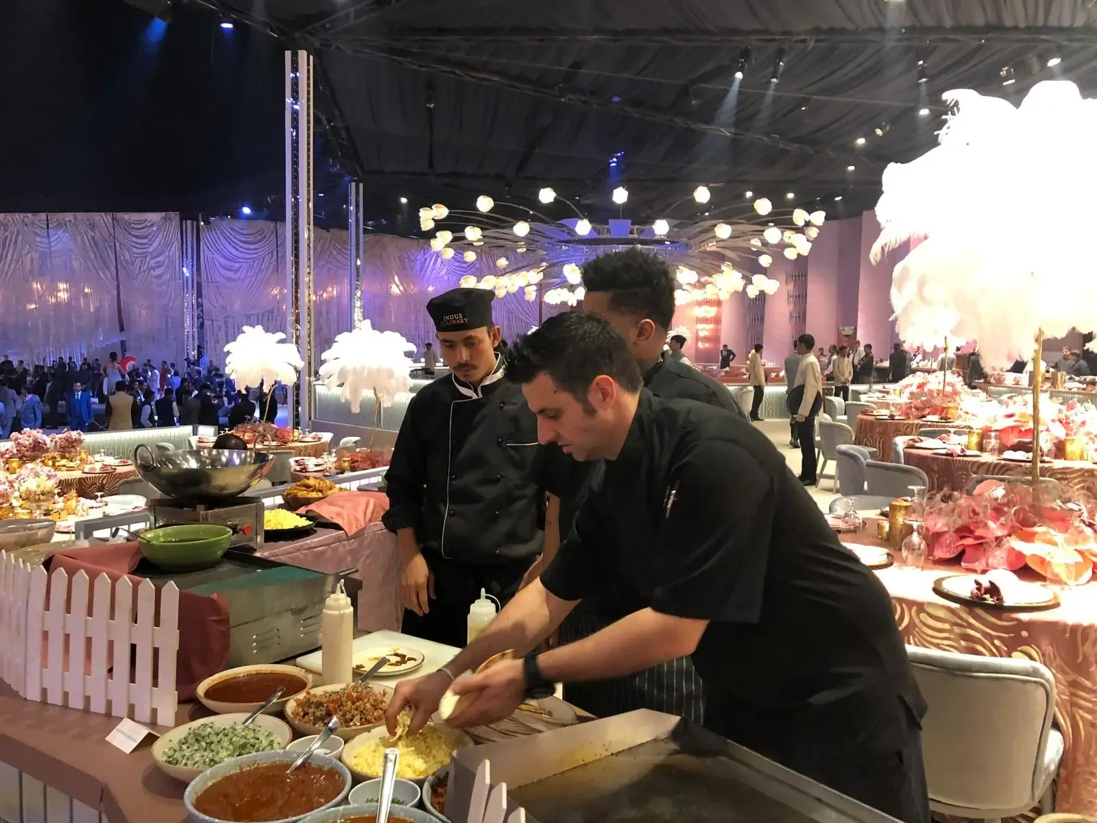 Chefs plating dishes at a live station in a large event hall
